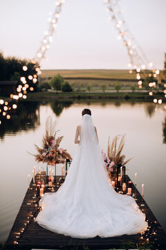 The bride stands on a pier by the lake at sunset
