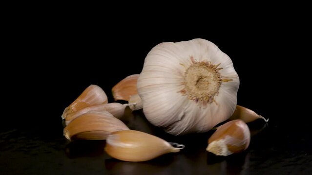 head of garlic surrounded by garlic cloves rotates on a black background 