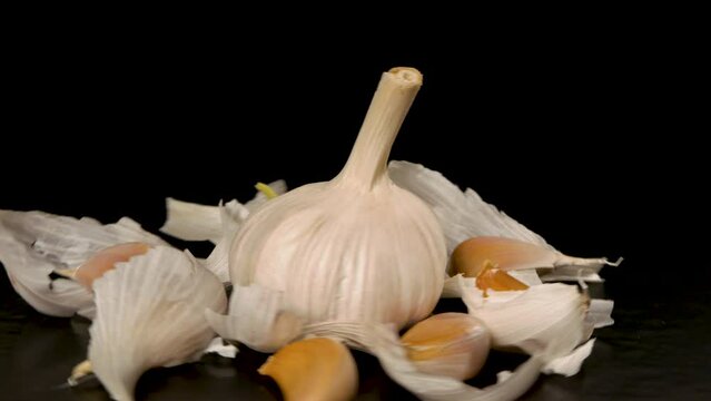 head of garlic surrounded by garlic cloves rotates on a black background 
