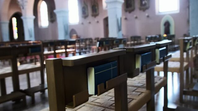 Wooden pews inside catholic cathedral, benches for prayers, ornament, interior. Empty Wooden chairs for church members. Inside an empty catholic church illuminated by sun rays. Small Chapel. 4K