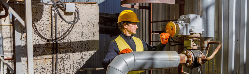 Matured man factory worker wearing work vest and gloves while standing near metal pipe