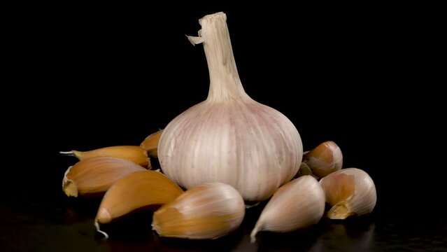 head of garlic surrounded by garlic cloves rotates on a black 