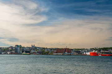 Naklejka premium St. John's, Newfoundland, Canada - March 2022: Colorful downtown St. John's with historic wooden residential, commercial, business,and Federal Government buildings. There are colorful ships docked.