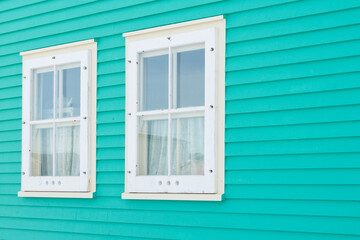 Two double hung windows on a green exterior wall of a vintage style building. The building has...