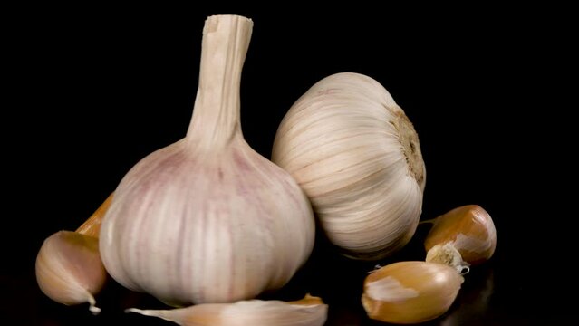 Two heads of garlic surrounded by garlic cloves, rotate on a black background 