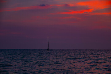 Fototapeta na wymiar Red sunset over the sea with sailboat in the distance