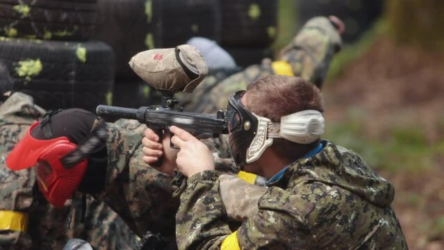 High-quality. Paintball sport player wears protective mask aiming gun. Shot from a paintball gun. Portrait of cheerful adult people playing war on the battlefield.