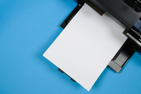 Top view of the printer and a blank sheet of a4 paper on a blue background