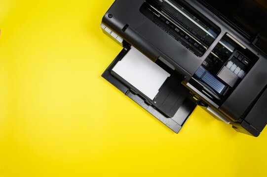 Top view of a photo printer and a blank sheet of photo paper on a yellow background