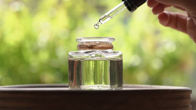 Drops of aromatherapy essential oil are falling from a dropper into a bottle, slow motion
