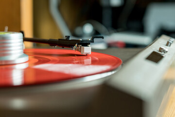 Fototapeta na wymiar Closeup view of a tonearm and turntable playing color red vinyl record.