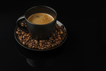 aromatic freshly brewed coffee in a black ceramic cup and coffee beans on a glass black surface
