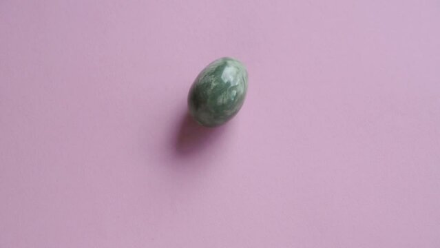 Green jade egg spinning on pink background with copy space, slow motion