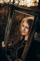 beautiful Ukrainian girl in black clothes near the old wooden house. The war in Ukraine. Portrait of a woman on a dark wooden background. Old abandoned wooden house. Old wooden window frame