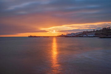 Obraz premium A beautiful sunrise bursts over the smooth sea at the old swanage pier