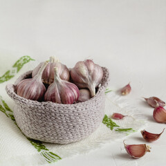 Organic purple garlic bulbs in a crochet basket on a linen cloth. Fresh garlic as a natural antibiotic.