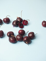 fresh ripe sweet cherries on a blue surface, one split in half showing its juicy purple interior flesh with seed