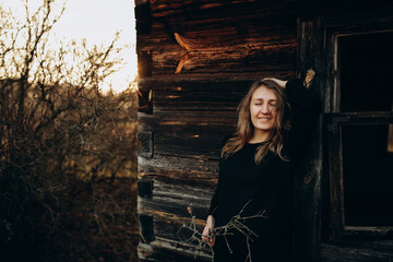 beautiful Ukrainian girl in black clothes near the old wooden house. The war in Ukraine. Portrait of a woman on a dark wooden background. Old abandoned wooden house. Old wooden window frame