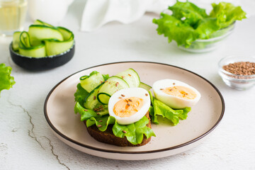 Appetizing bruschetta from rye bread, lettuce, cucumber, boiled egg and flax seeds on a plate on the table. Healthy eating on a diet.