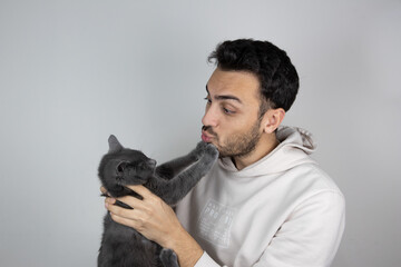Young man holding and kissing cat on gray isolated background. Care and maintenance of pets.