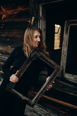 beautiful Ukrainian girl in black clothes near the old wooden house. The war in Ukraine. Portrait of a woman on a dark wooden background. Old abandoned wooden house. Old wooden window frame