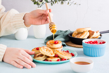 Children's hands pour honey over pancakes and cranberries on a plate. Homemade breakfast dessert