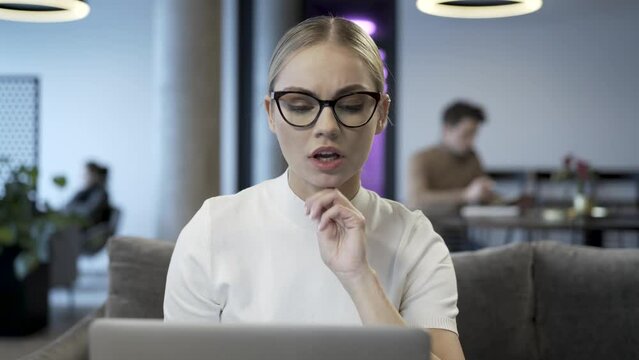 Young and confident businesswoman is sitting in front of laptop computer and look to the screen. Person is reading text, watching video, looking for image or search data library for information source