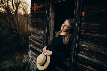 Obraz na płótnie Canvas beautiful Ukrainian girl in black clothes near the old wooden house. The war in Ukraine. Portrait of a woman on a dark wooden background. Old abandoned wooden house. Old wooden window frame