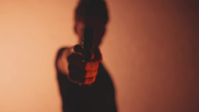 Silhouette of anonymous man pointing a hand gun towards the camera 