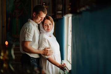 man and woman in headscarf and light-colored robes by window in church. 