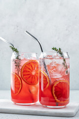 Blood Orange lemonade cocktail with ice and thyme on light gray concrete background
