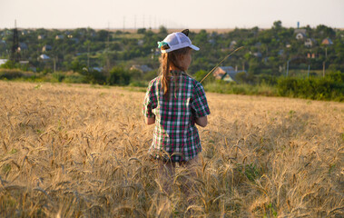 Naklejka na ściany i meble girl in a cap and a country-style shirt in a ripened wheat field at sunset. summer evening walk outdoors