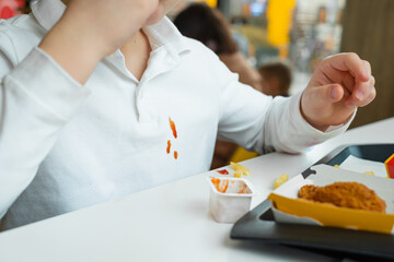 Close up of dirty ketchup stains on white kid clothes. Boy eating french fries potato chips and tomato sauce at the table in a fast food restaurant.