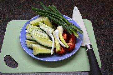 sliced fresh cucumbers, tomatoes and onions on a plate, next to a kitchen knife and a cutting board. the concept of proper nutrition and vegetarianism