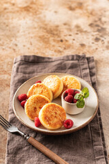 Cottage cheese fritters syrniki with honey topping and raspberry and mint on ceramic plate on napkin on textured background. Text space