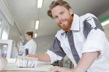 man brushing glue paste onto wallpaper on desk