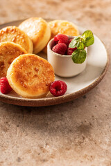 Cottage cheese pancakes, syrniki with honey topping and raspberry and mint on ceramic plate on textured background. Text space