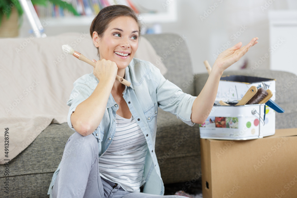 Wall mural jovial woman sat on the floor holding a paintbrush