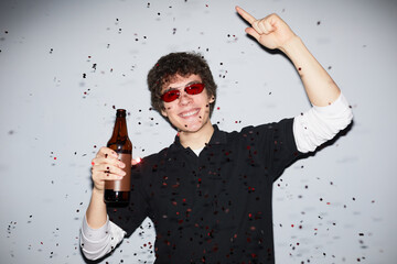 Waist up portrait of smiling young man partying and looking at camera holding beer, shot with flash