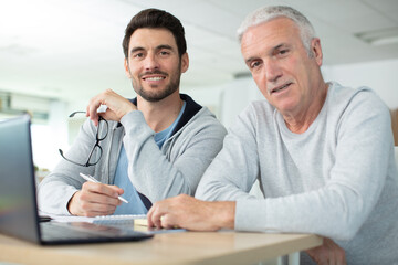 adult son helping senior father with computer at home