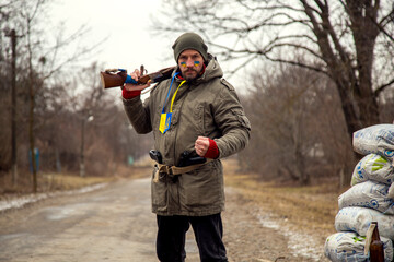 A Ukrainian man with a weapon at a checkpoint. A Ukrainian patriot guards the entrance to his...