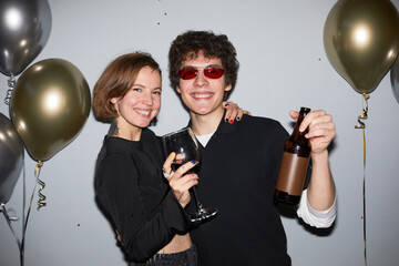 Waist up portrait of smiling young couple partying and looking at camera holding drinks, shot with flash