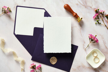 Elegant wedding stationery set. Wedding invitation card template, purple envelopes, silk ribbon, rings, pink flowers on stone desk table. Flat lay, top view, copy space.