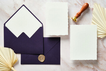 Wedding stationery top view. Flat lay blank white invitation cards, purple envelopes, wedding decorations and dried flowers on marble table.