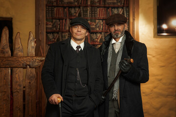 Two men of different ages, English retro gangster of the 1920s dressed in a coat, suit and flat cap...