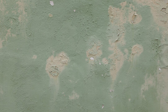 Old weathered painted wall background texture. Green dirty peeled plaster wall with falling off flakes of paint. House wall eroded due to humidity and sunlight.