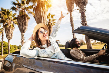Happy young couple having enjoying summer vacation on convertible car - Man and woman laughing while driving a cabriolet auto outdoors - Travel, car rental service and holidays concept - obrazy, fototapety, plakaty