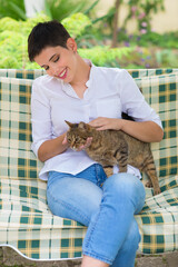 Young woman sitting in the deck chair with her cat on a sunny summer day.