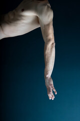 Crop muscular hand and torso of faceless male with arm stretching on dark background.