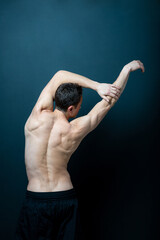 Back view of faceless muscular shirtless acrobat male dancer stretching his arms.